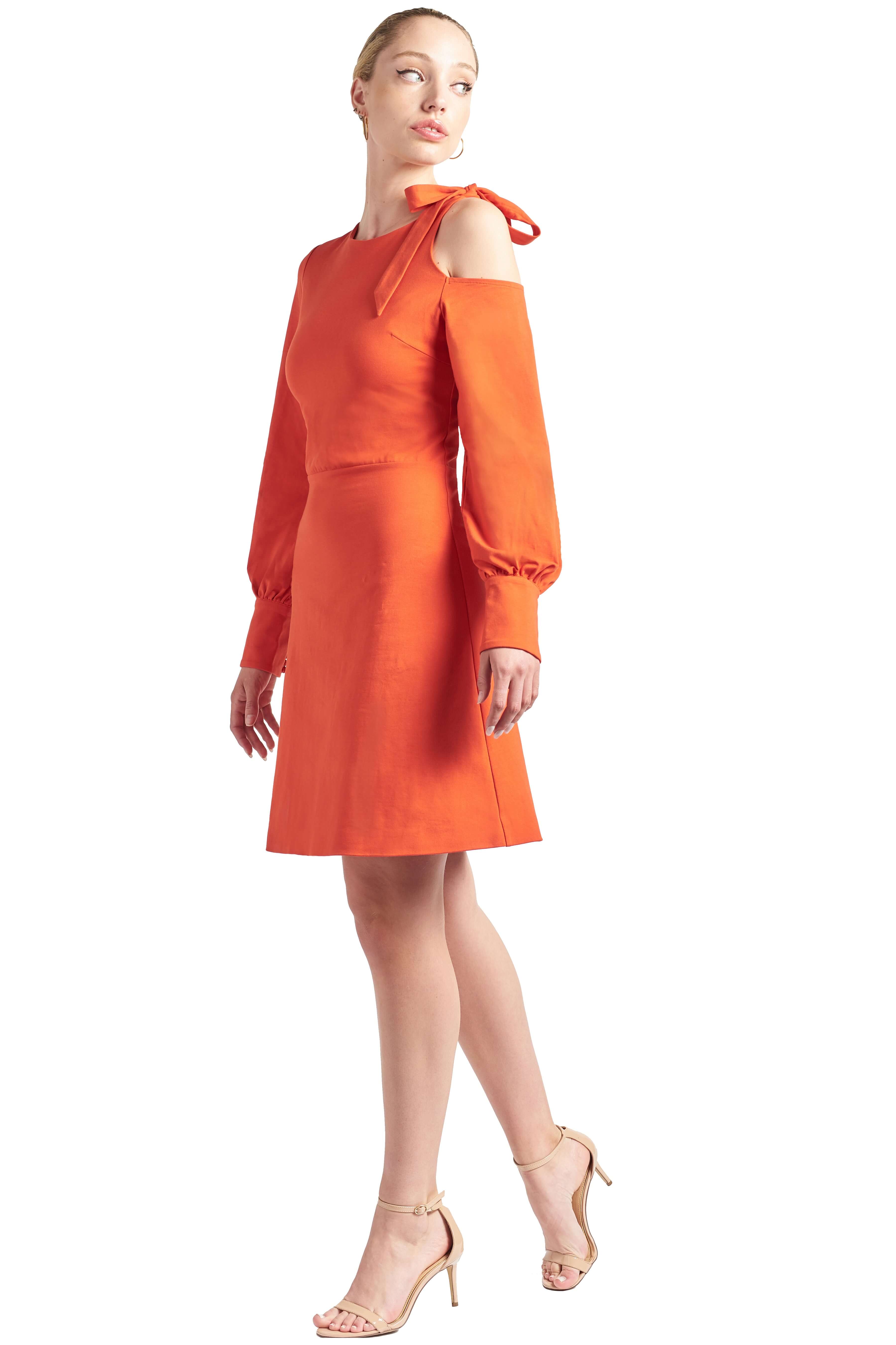 Model wearing fit & flare orange colored long sleeve dress with single shoulder cut-out and shoulder bow-tie.