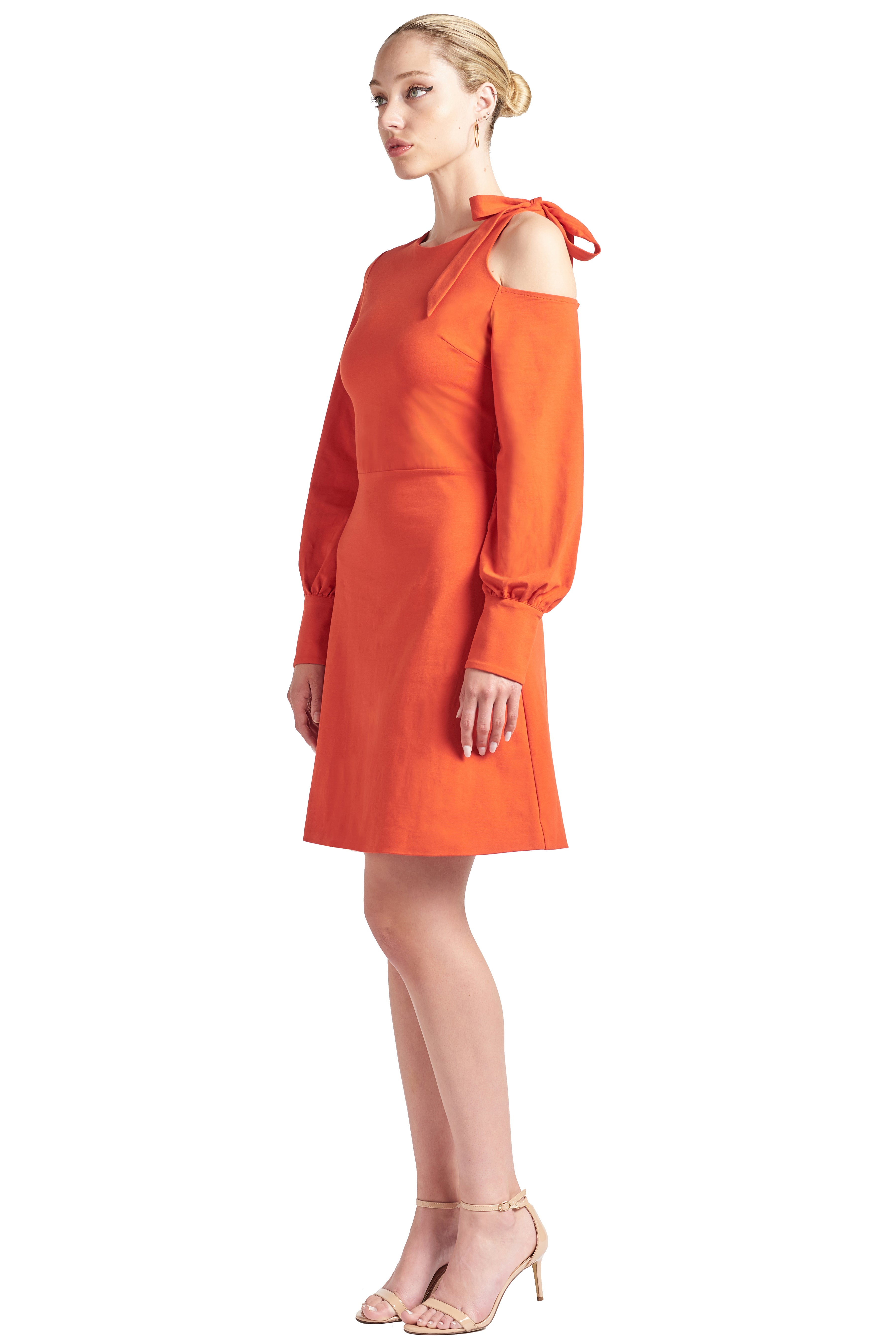 Model wearing fit & flare orange colored long sleeve dress with single shoulder cut-out and shoulder bow-tie.
