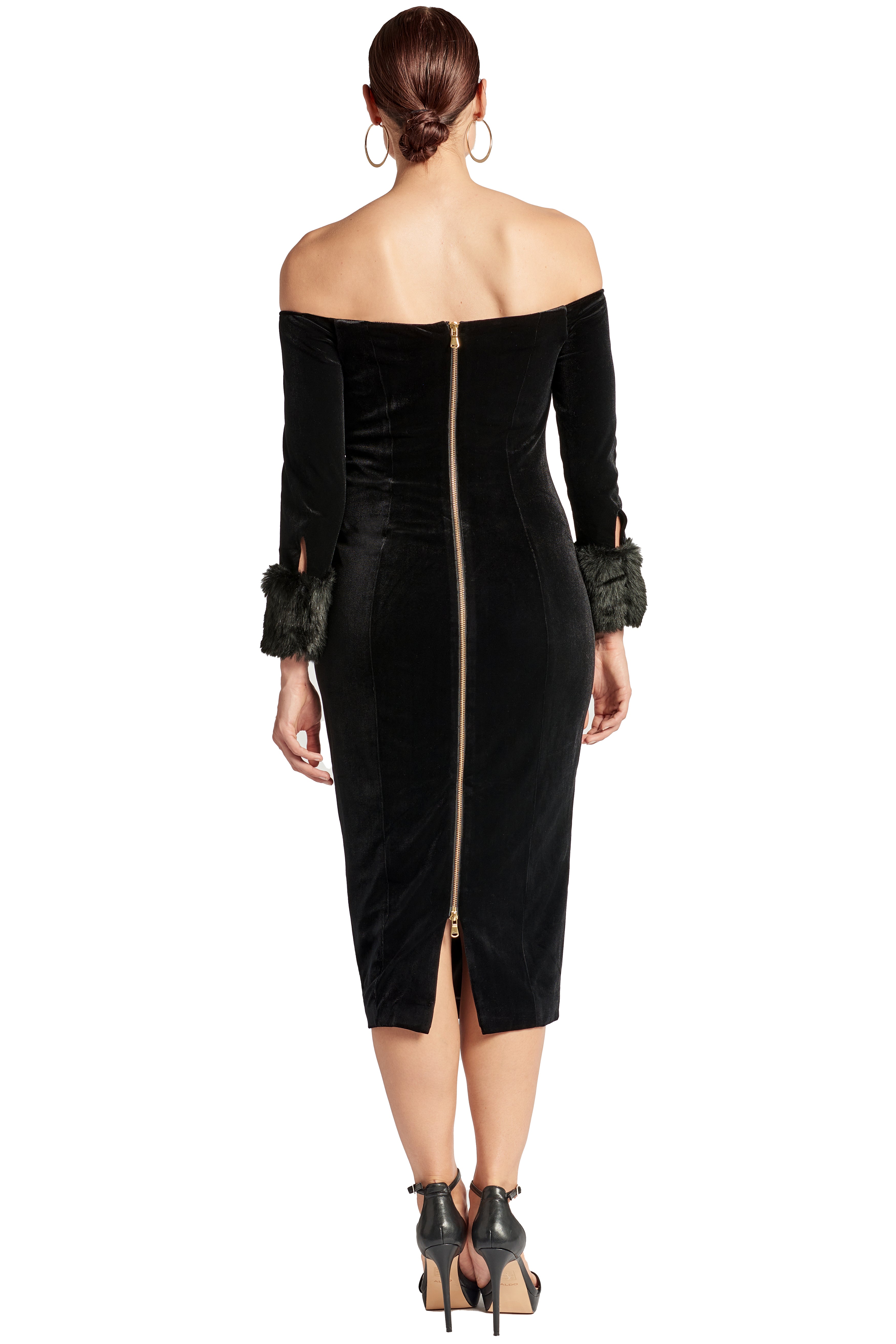 Back view of model wearing the Simona Maghen Joia Dress, off the shoulder black velvet fitted midi dress with long sleeves and faux fur cuffs, with an exposed gold zipper down the center back.
