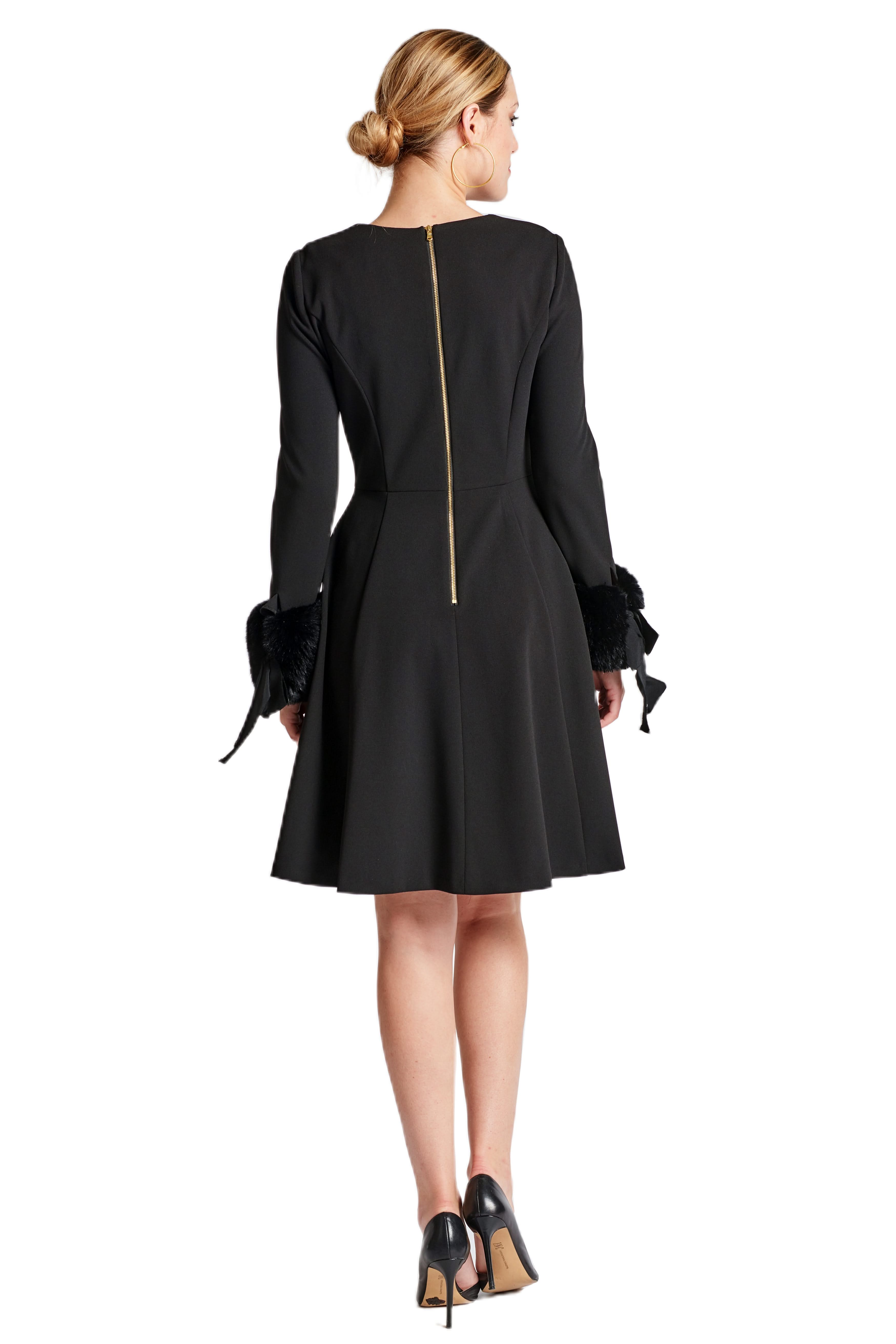 Back view of a model wearing a black fit & flare dress with long sleeves, faux fur cuffs and a gold zipper.