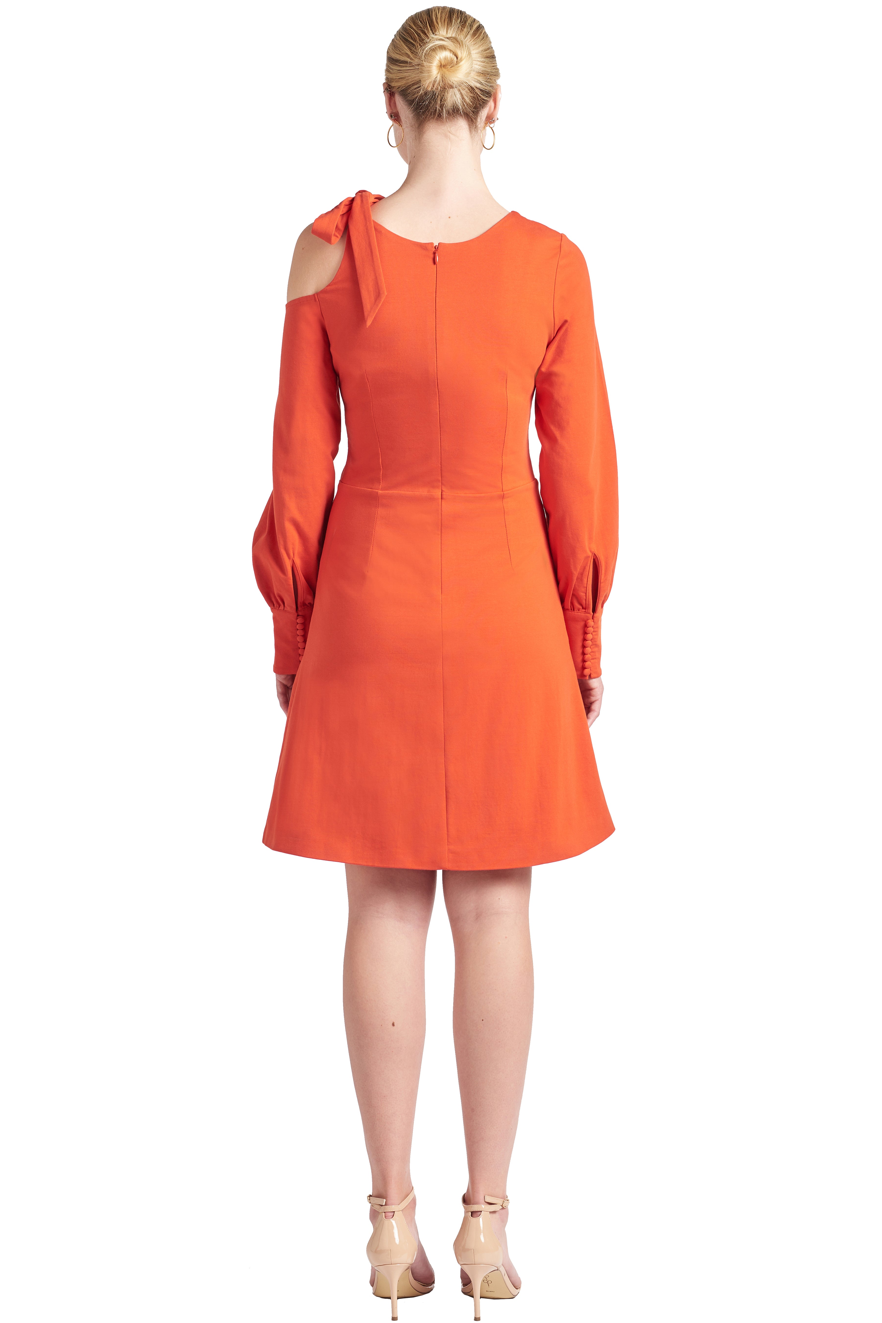 Back view of model wearing fit & flare orange colored long sleeve dress with single shoulder cut-out and shoulder bow-tie.