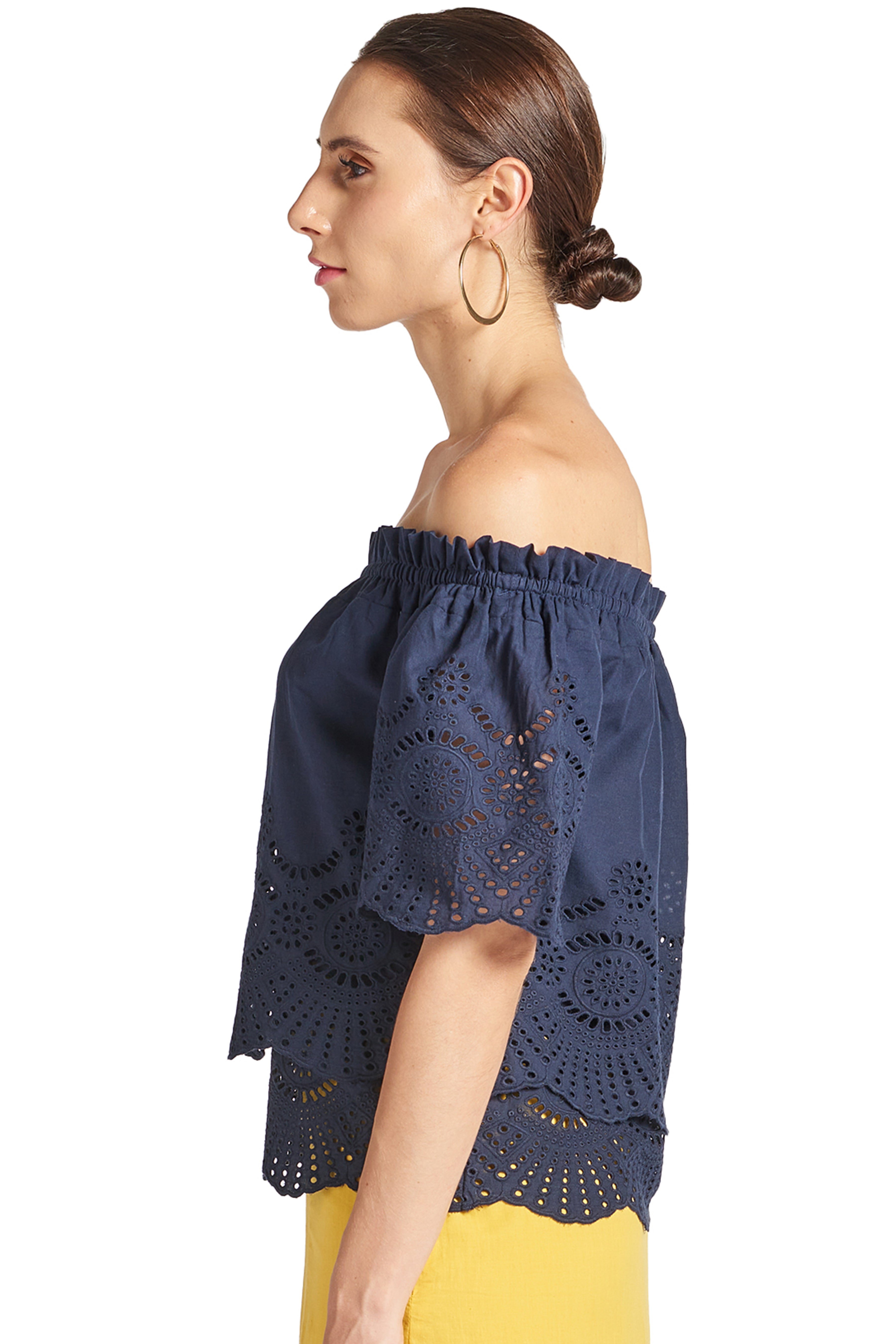 Side view of model wearing navy off the shoulder cotton eyelet top with scalloped short sleeves and scalloped bottom hem.