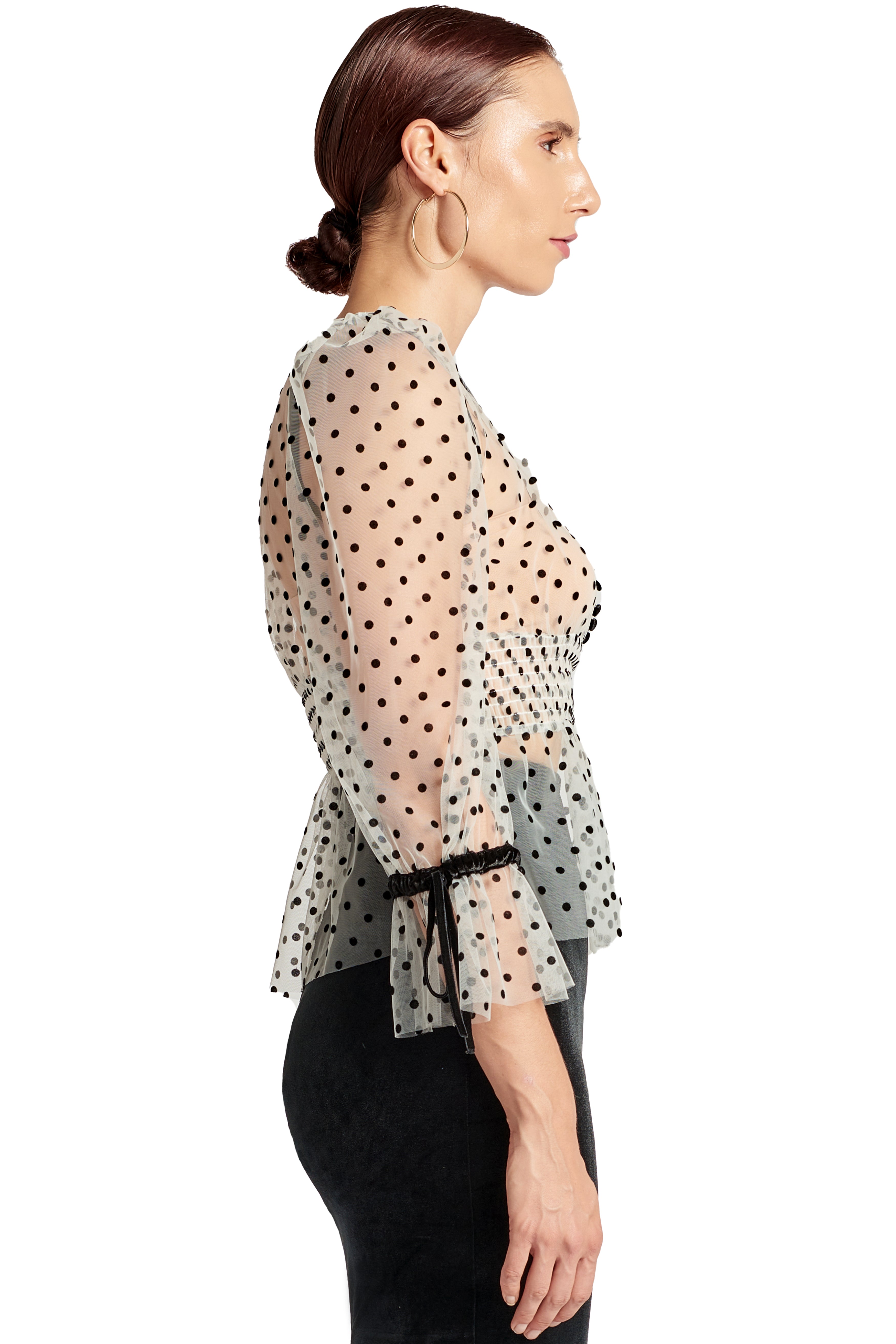 Side view of model wearing the Simona Maghen J'lene Top, white mesh black polka dot 3/4 puff sleeve peplum hem v-neck top with black velvet buttons and bows.