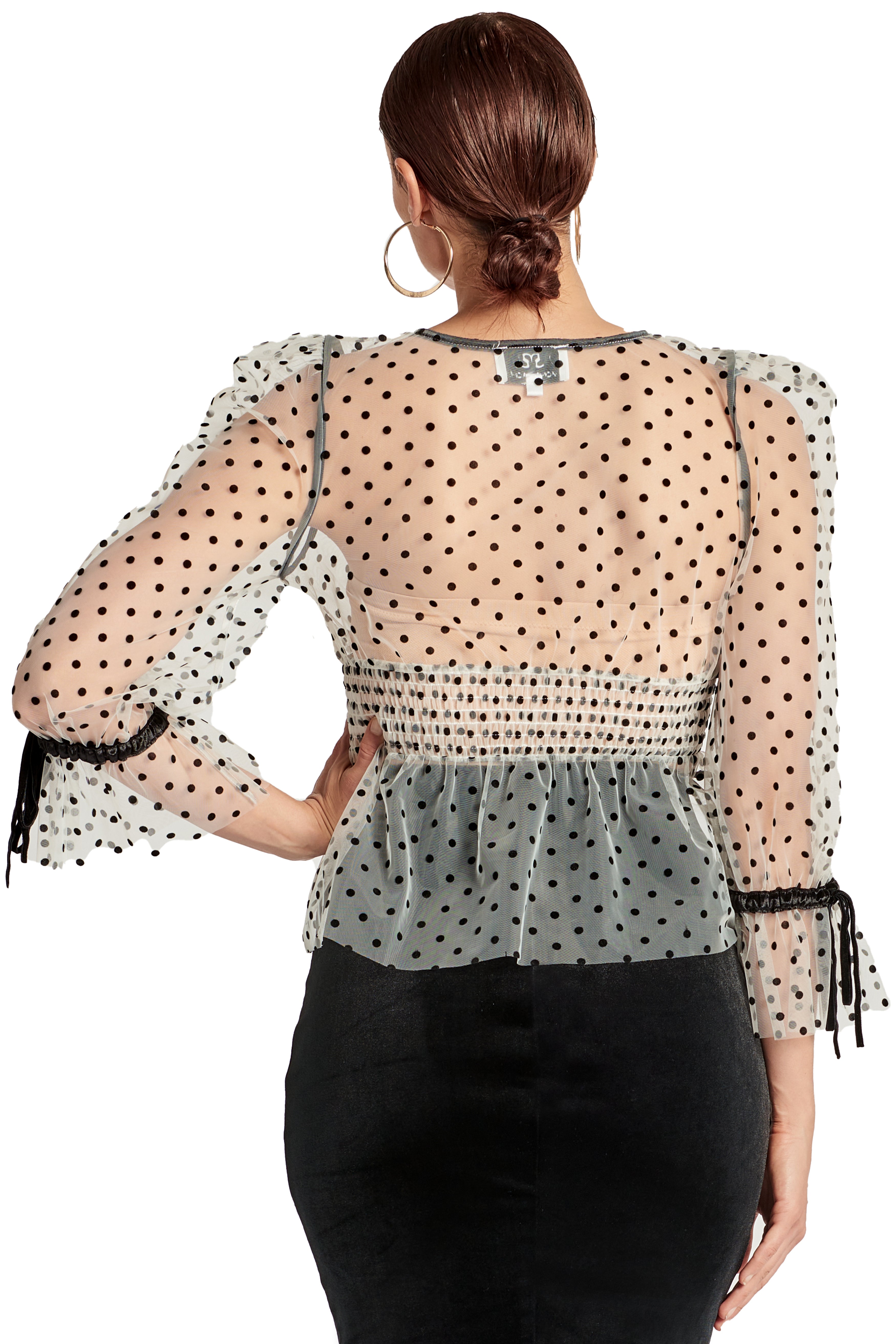 Back view of model wearing the Simona Maghen J'lene Top, white mesh black polka dot 3/4 puff sleeve peplum hem v-neck top with black velvet buttons and bows.