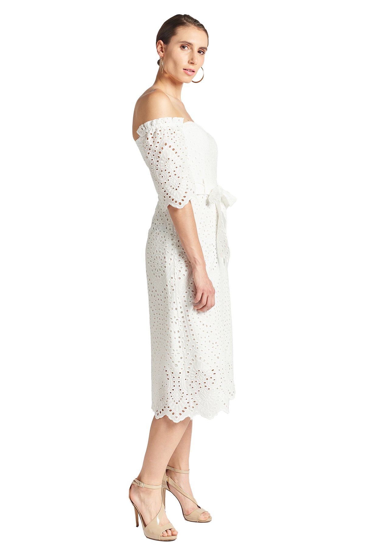 Side view of model wearing the Simona Maghen Jasmine Dress, white cotton scalloped eyelet midi a-line dress with off the shoulder sweetheart neckline, self belt, and short sleeves.