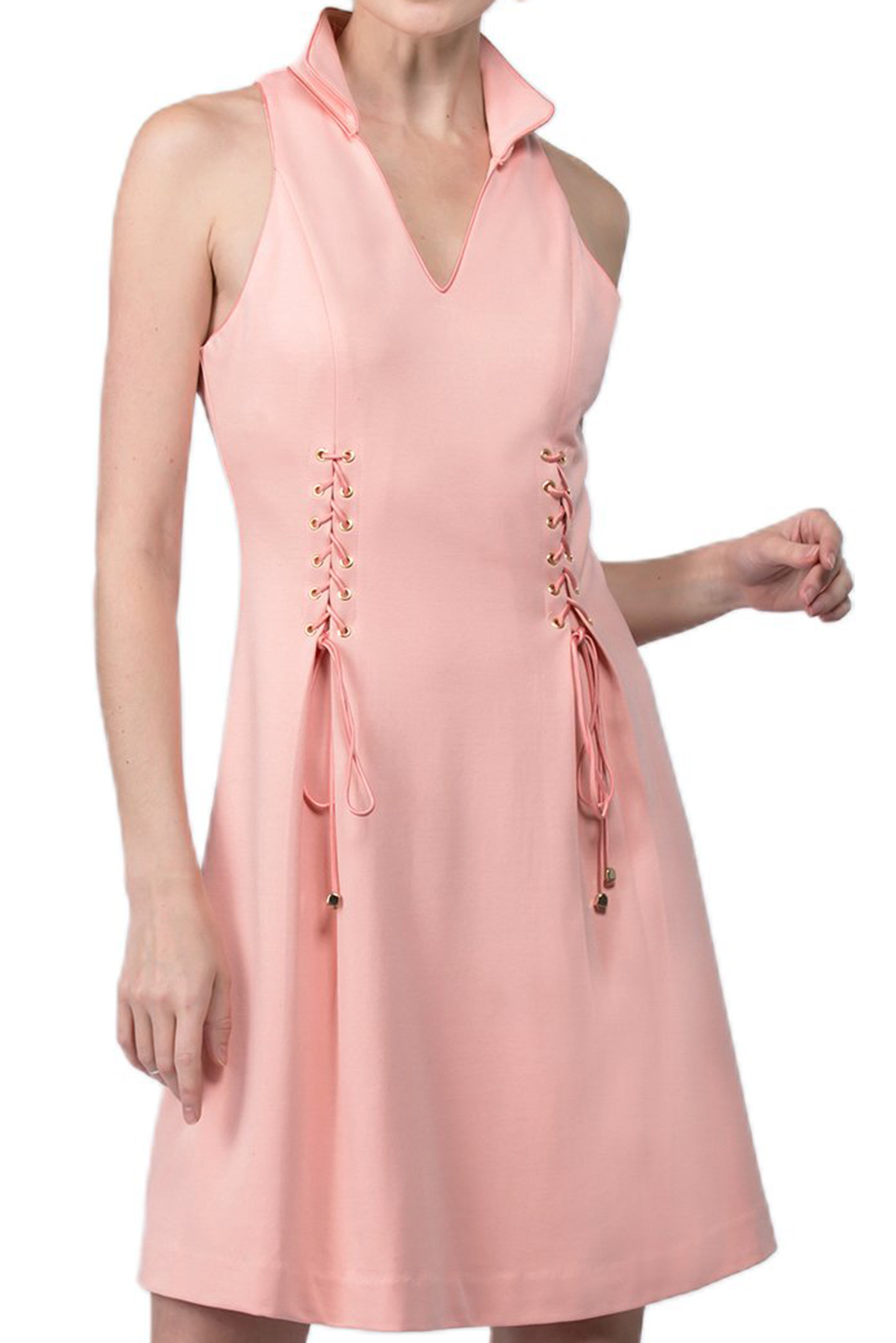 Close-up view of model wearing sleeveless racer neck peachy pink short fit and flare wing tip collar dress with corset lace up ties at front waist.