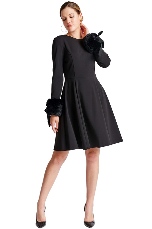 Woman in black fit & flare dress with long sleeves and faux fur cuffs.