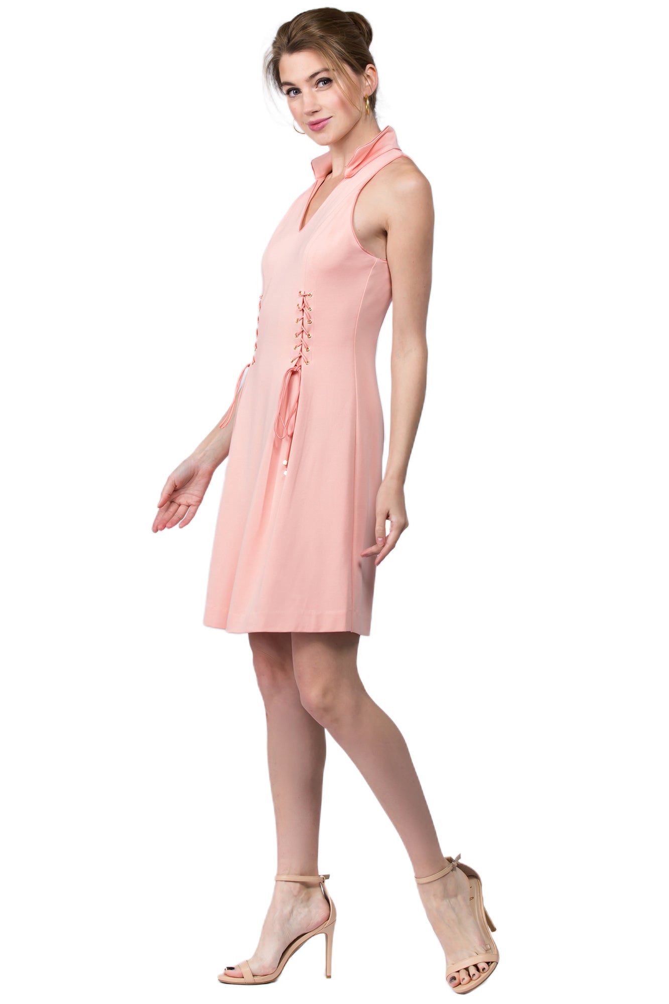 3/4 front view of model wearing sleeveless racer neck peachy pink short fit and flare wing tip collar dress with corset lace up ties at front waist.