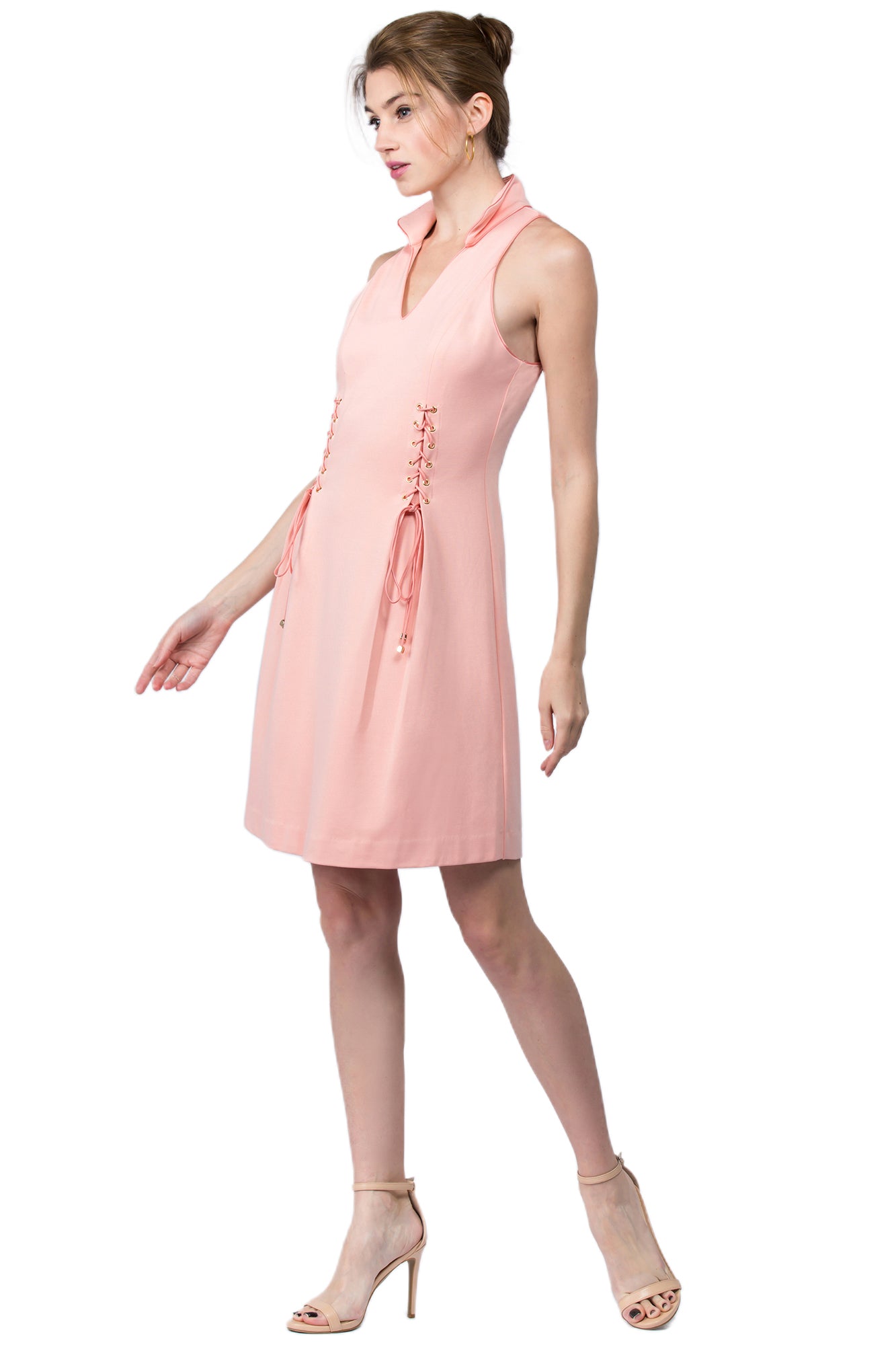 3/4 front view of model wearing sleeveless racer neck peachy pink short fit and flare wing tip collar dress with corset lace up ties at front waist.